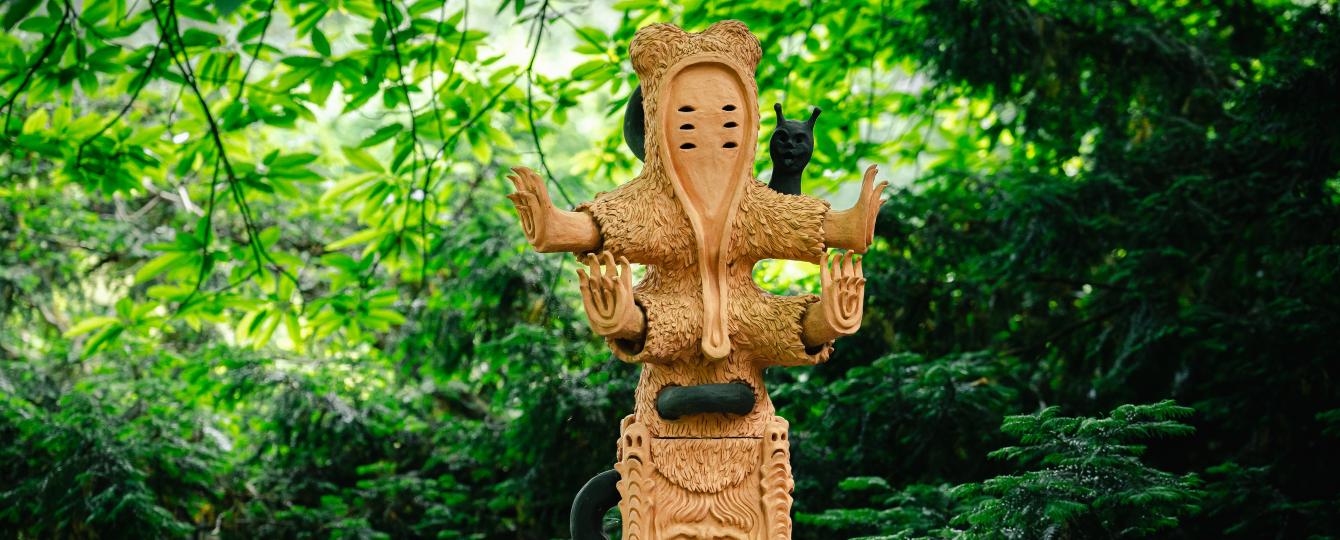 Frontaal zicht op kunstwerk The Voyage of the Mascot van Sharon Van Overmeiren met op de achtergrond het groen van struiken en bomen.