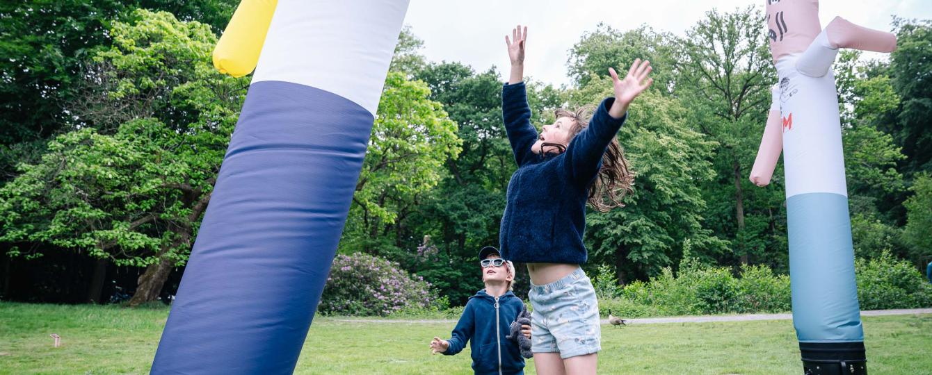 Jongen en meisje springen naar een van de skytubes uit het kunstwerk The Pogo Never Stops van Dennis Tyfus, opgesteld in het kunstpark van het Middelheimmuseum.
