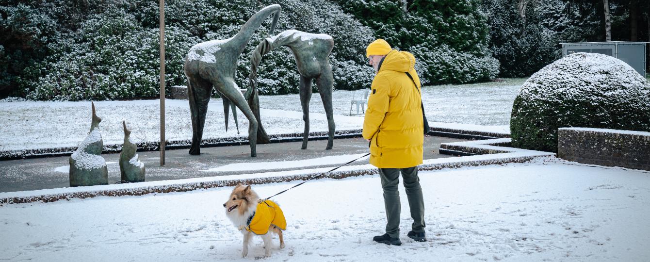 Winterlandschap met bezoeker in gele jas en hond in gele jas bij fontein Camille Henrot