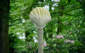 Schelpvormige sculptuur in rocaille op een hoge paal omgeven door een groene boomkruin