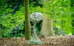 Grillige aluminium bloem omgeven door een bladertapijt en bomen