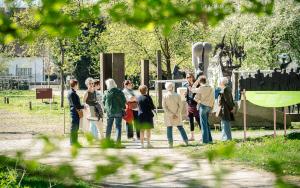 Zicht door het groene gebladerte op gids met groep aan het openluchtdepot van het Middelheimmuseum 
