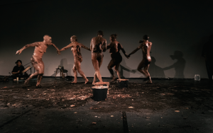 5 met klei ingesmeerde dansende performers op podium