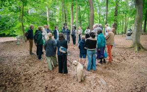 Sfeerbeeld met bezoekers in kring rond gids en kunstwerk in het kunstpark van het Middelheimmuseum.
