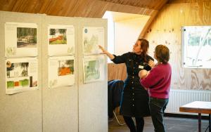 Sfeerbeeld van medewerker die uitleg geeft bij infopanelen met prints aan bezoeker met baby op de arm in Atelier van Lieshout.