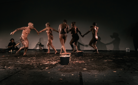 5 met klei ingesmeerde dansende performers op podium