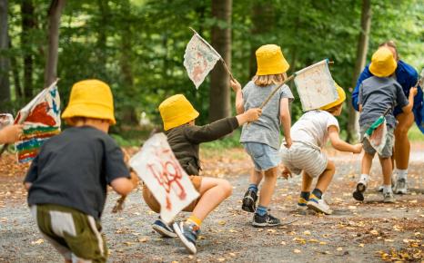 Kleine kinderen met gele hoedjes en zwaaiend met vlaggetjes stappend achter elkaar in het kunstpark