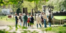 Zicht door het groene gebladerte op gids met groep aan het openluchtdepot van het Middelheimmuseum 