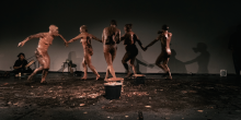5 met klei ingesmeerde dansende performers op podium