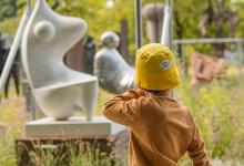 Kind in zomeroutfit en met geel zonnehoedje van Coccolarte wandelend langs het openluchtdepot in het kunstpark