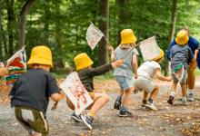 Kleine kinderen met gele hoedjes en zwaaiend met vlaggetjes stappend achter elkaar in het kunstpark