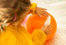 Sfeerbeeld van jong kind met gele schort en knutselend met oranje ballon en wit papier-maché